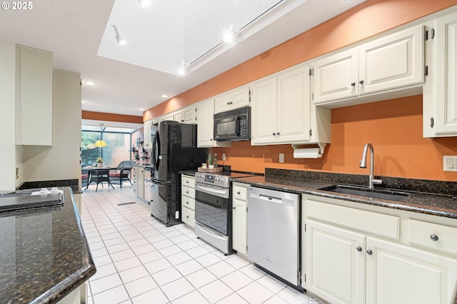 kitchen with dark stone counters, sink, appliances with stainless steel finishes, light tile patterned flooring, and white cabinetry