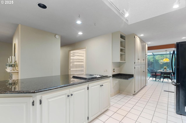 kitchen with white cabinetry, black fridge, kitchen peninsula, dark stone counters, and light tile patterned floors