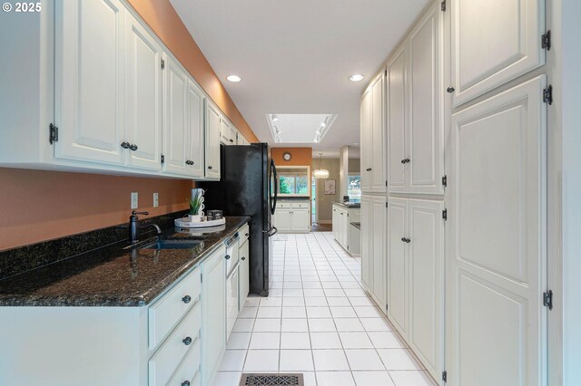 kitchen featuring dark stone counters, sink, white cabinets, and light tile patterned flooring