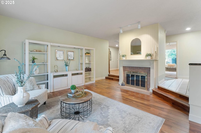 living room featuring baseboards, recessed lighting, wood finished floors, a brick fireplace, and rail lighting