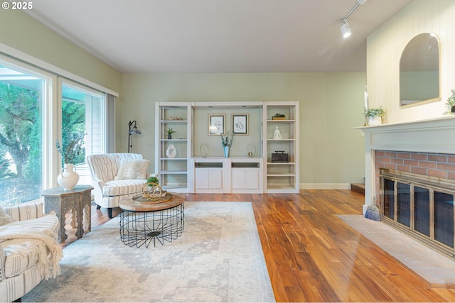 living area featuring track lighting, wood finished floors, a brick fireplace, and baseboards