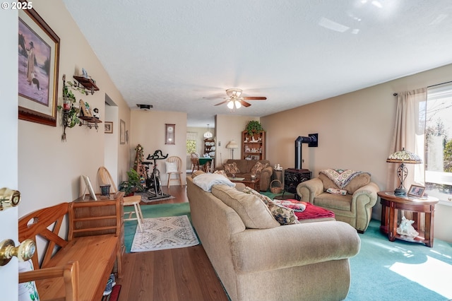 living room featuring wood-type flooring, a wood stove, ceiling fan, and a textured ceiling