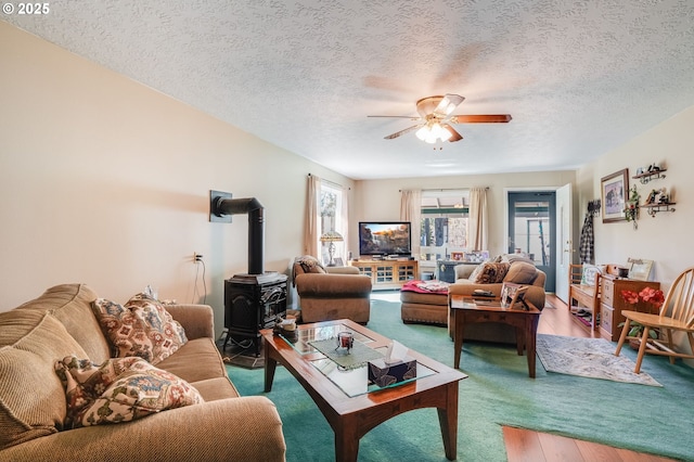 living room featuring hardwood / wood-style flooring, a textured ceiling, ceiling fan, and a wood stove