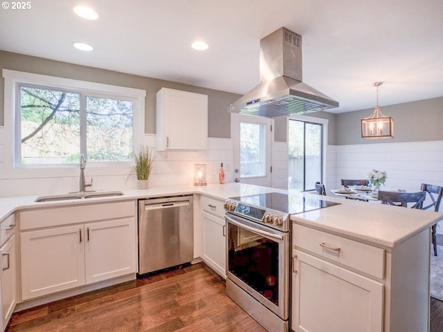 kitchen featuring island exhaust hood, appliances with stainless steel finishes, a sink, a peninsula, and dark wood-type flooring