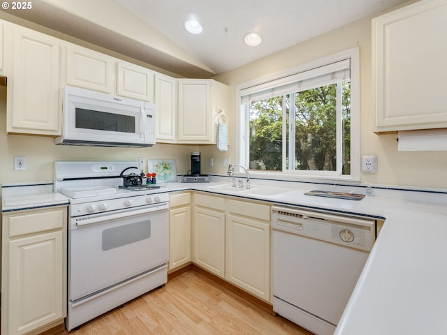 kitchen with white appliances, a sink, light countertops, vaulted ceiling, and light wood finished floors
