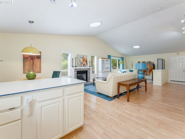living room featuring vaulted ceiling, a fireplace with raised hearth, and light wood-style flooring