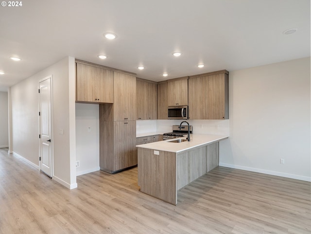 kitchen with appliances with stainless steel finishes, sink, kitchen peninsula, and light hardwood / wood-style flooring