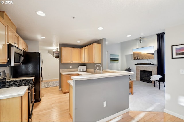 kitchen with stainless steel appliances, a fireplace, light brown cabinets, kitchen peninsula, and light wood-type flooring