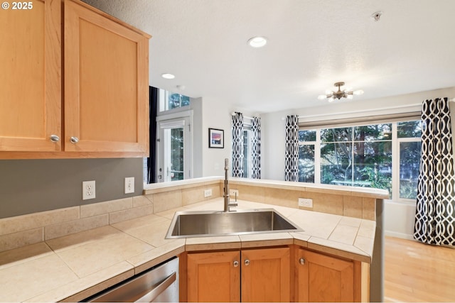 kitchen with sink, an inviting chandelier, tile countertops, stainless steel dishwasher, and kitchen peninsula