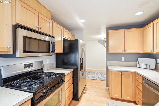 kitchen with stainless steel appliances, light brown cabinetry, and light hardwood / wood-style floors