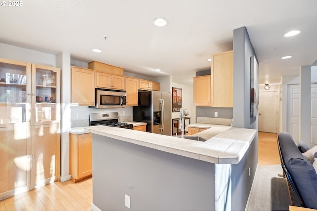 kitchen featuring appliances with stainless steel finishes, kitchen peninsula, light hardwood / wood-style floors, and light brown cabinets