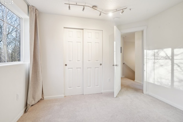 unfurnished bedroom featuring track lighting, light carpet, and a closet