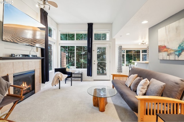 living room with ceiling fan, a tiled fireplace, light carpet, and a wealth of natural light