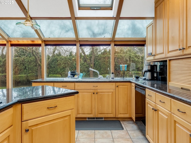 kitchen with a skylight, light tile patterned floors, a sink, dark stone countertops, and dishwasher