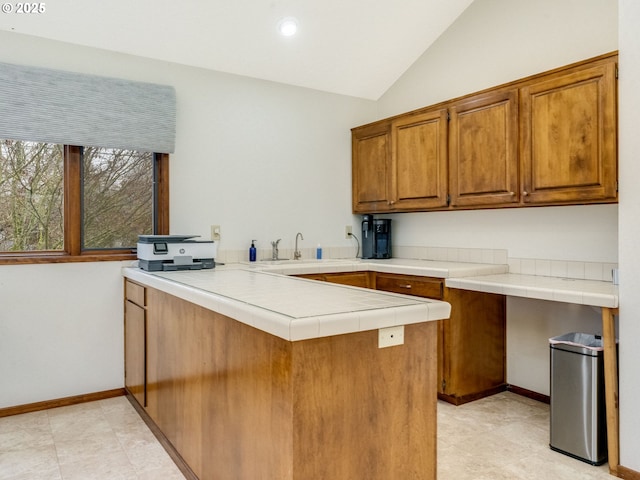 kitchen with baseboards, tile countertops, brown cabinets, a peninsula, and vaulted ceiling