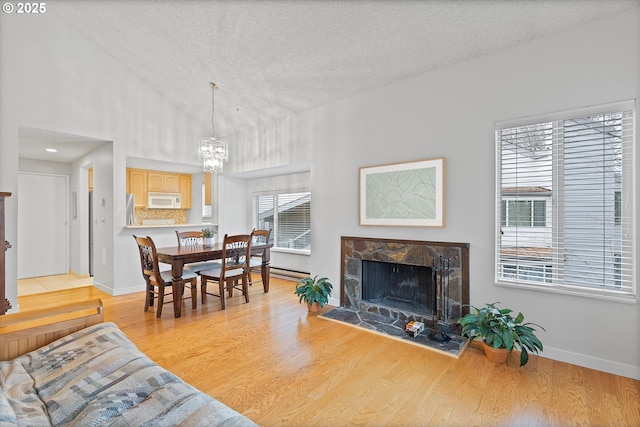 living area with baseboards, a textured ceiling, light wood-type flooring, a fireplace, and a chandelier