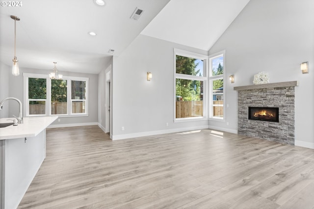 unfurnished living room with light hardwood / wood-style floors, sink, a fireplace, and vaulted ceiling