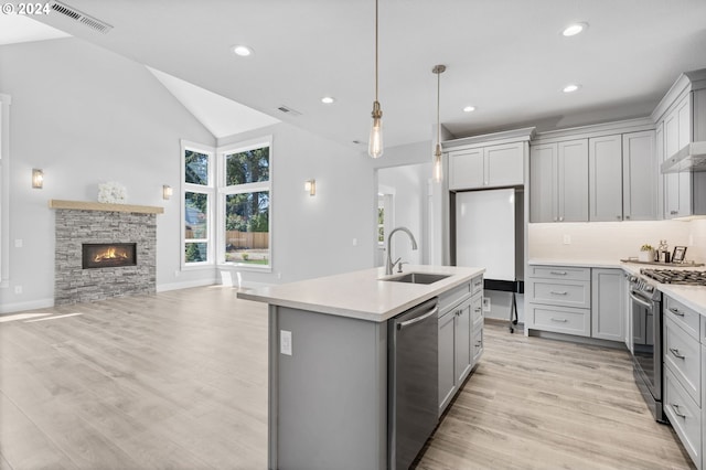 kitchen with stainless steel appliances, a kitchen island with sink, sink, a stone fireplace, and lofted ceiling