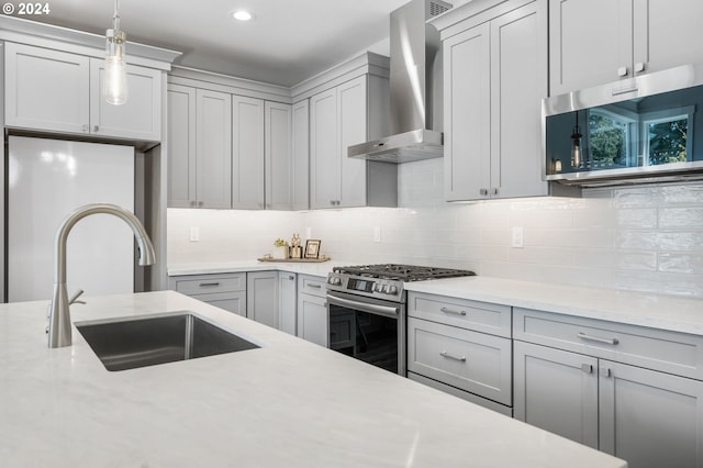 kitchen featuring light stone counters, wall chimney exhaust hood, stainless steel appliances, sink, and hanging light fixtures