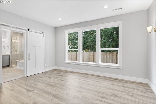 unfurnished bedroom featuring a barn door, light hardwood / wood-style floors, and connected bathroom