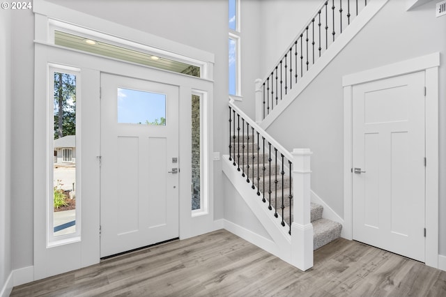 foyer featuring baseboards, visible vents, light wood-style flooring, a high ceiling, and stairs