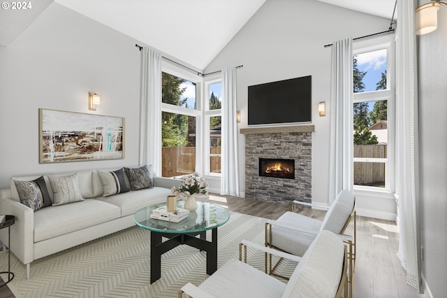 living area with high vaulted ceiling, light wood-type flooring, a fireplace, and baseboards