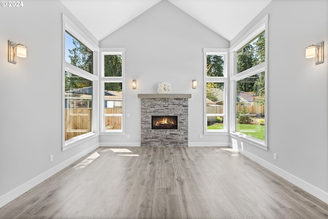 unfurnished living room with a healthy amount of sunlight, a stone fireplace, high vaulted ceiling, and light hardwood / wood-style flooring