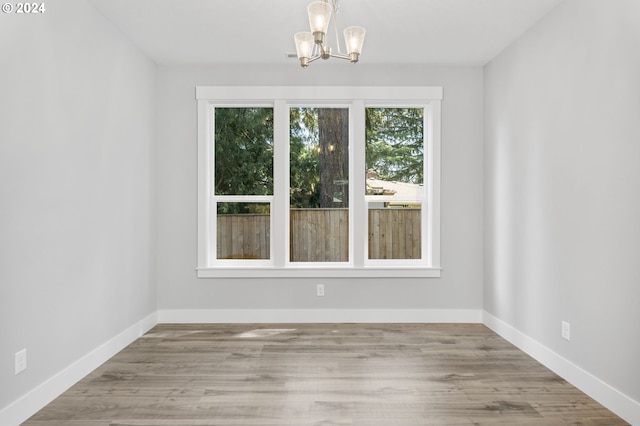 unfurnished dining area featuring light wood-type flooring, an inviting chandelier, and baseboards