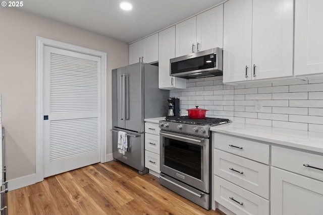 kitchen featuring light stone counters, light wood-type flooring, stainless steel appliances, decorative backsplash, and white cabinets