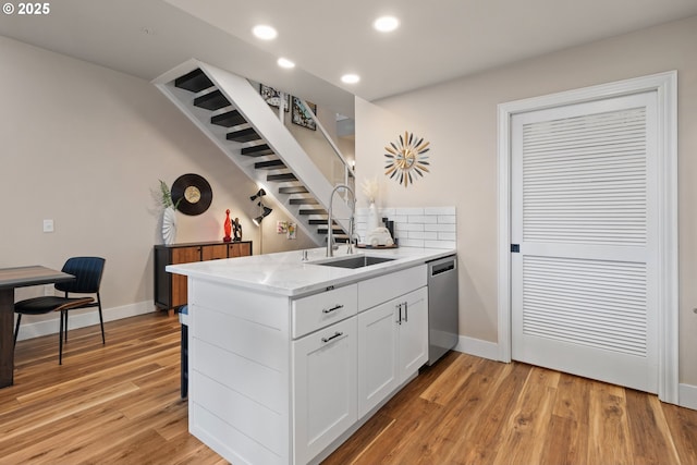 kitchen with sink, light hardwood / wood-style floors, light stone countertops, white cabinets, and stainless steel dishwasher