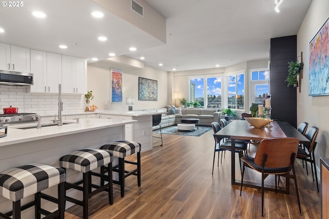 kitchen with a breakfast bar area, tasteful backsplash, appliances with stainless steel finishes, dark hardwood / wood-style flooring, and white cabinets