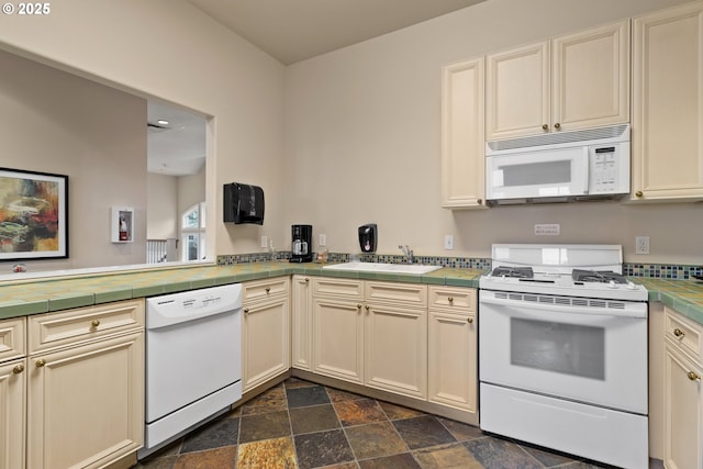 kitchen with cream cabinets, sink, tile counters, and white appliances