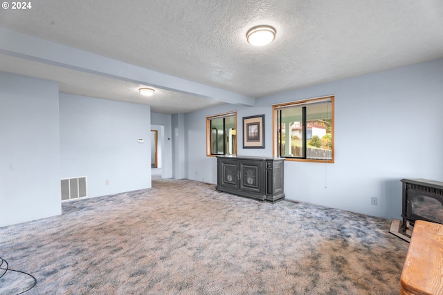 unfurnished living room featuring a wood stove, a textured ceiling, and carpet floors