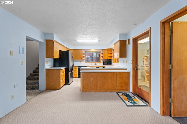 kitchen featuring freestanding refrigerator, light colored carpet, light countertops, a peninsula, and a textured ceiling