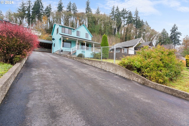 view of front facade with a porch, asphalt driveway, a carport, and fence