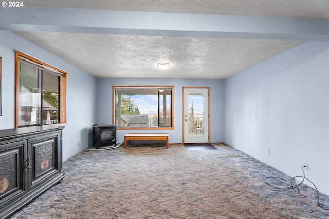 unfurnished living room with a wood stove, carpet flooring, and a textured ceiling