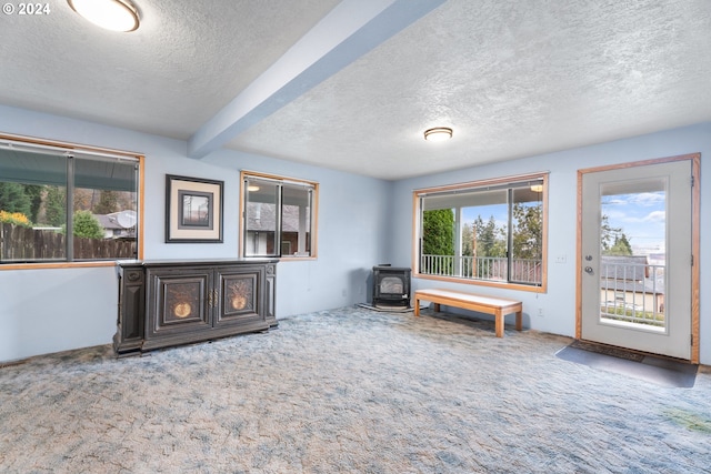 living area with a wood stove, a textured ceiling, carpet flooring, and beamed ceiling