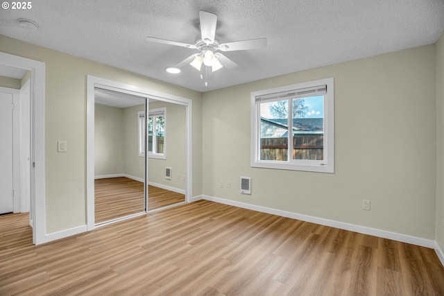 unfurnished bedroom with multiple windows, a textured ceiling, light hardwood / wood-style floors, and a closet