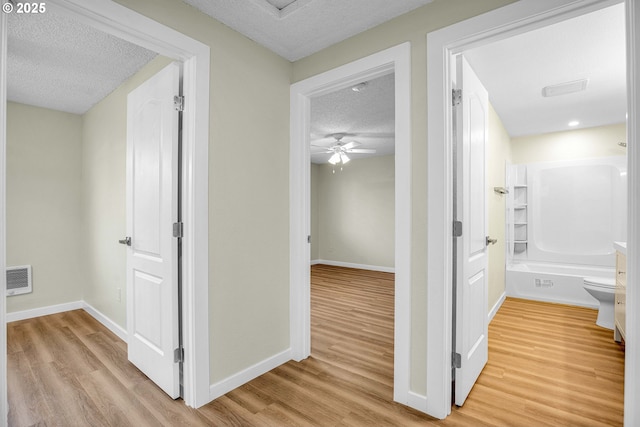 hallway with a textured ceiling and light hardwood / wood-style flooring