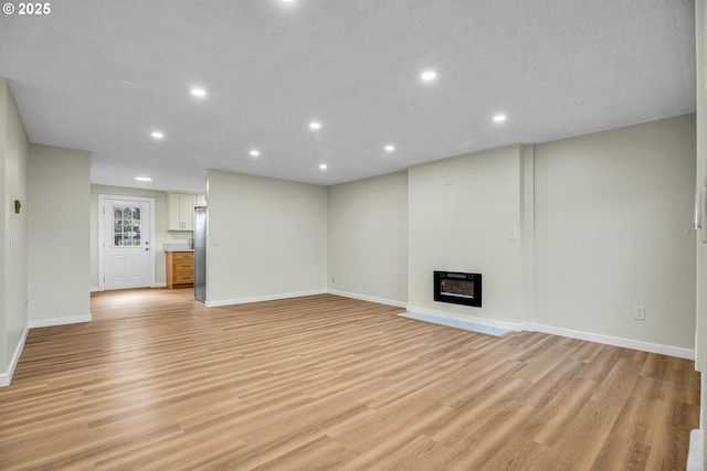 unfurnished living room featuring heating unit, a textured ceiling, and light hardwood / wood-style floors