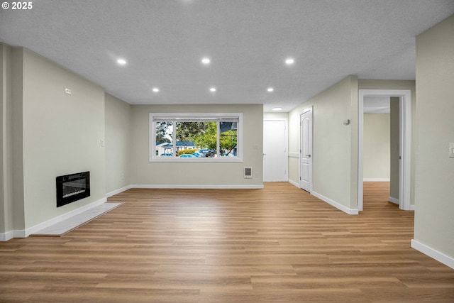 unfurnished living room with heating unit, a textured ceiling, and light hardwood / wood-style flooring