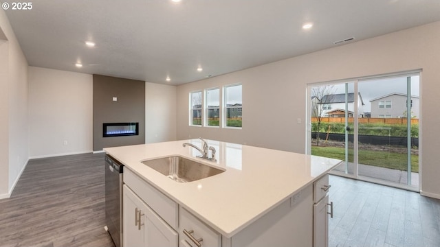 kitchen featuring dishwasher, white cabinetry, wood-type flooring, sink, and a kitchen island with sink