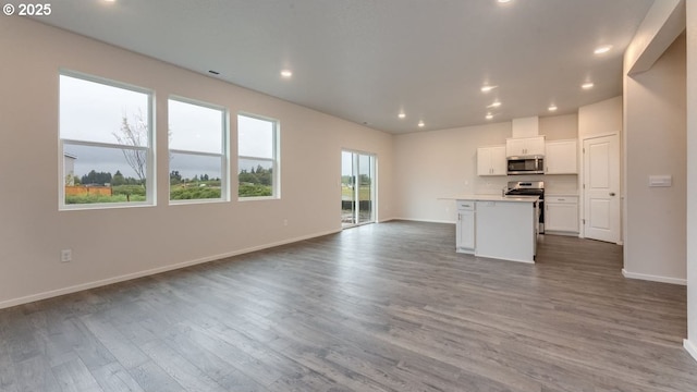 kitchen with an island with sink, appliances with stainless steel finishes, wood-type flooring, and white cabinets