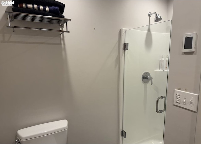 bathroom featuring a shower with door and toilet