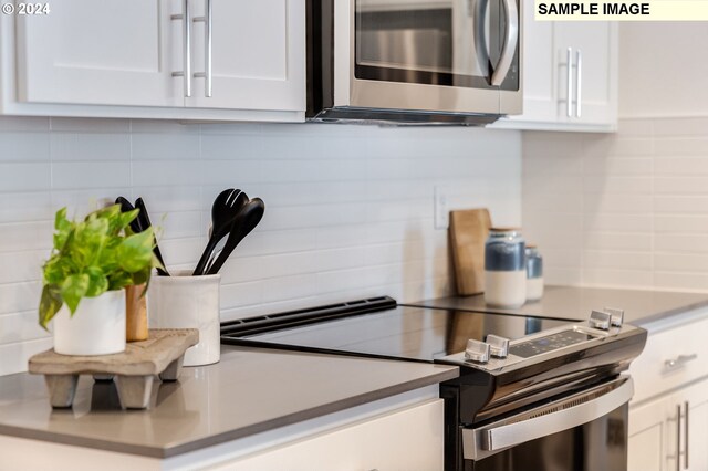 kitchen featuring stainless steel microwave, white cabinets, backsplash, and range with electric stovetop