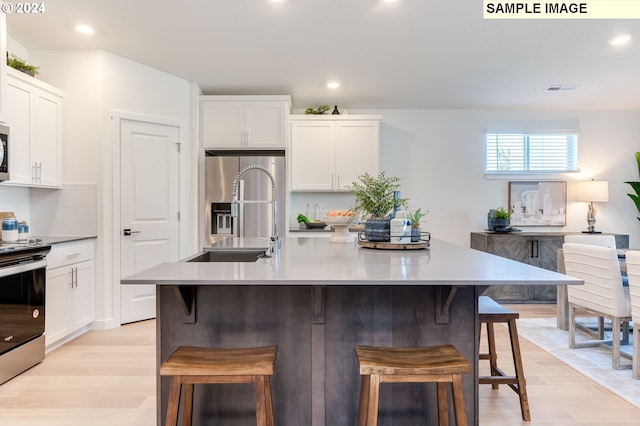 kitchen with stainless steel appliances, a center island with sink, white cabinets, and a kitchen bar