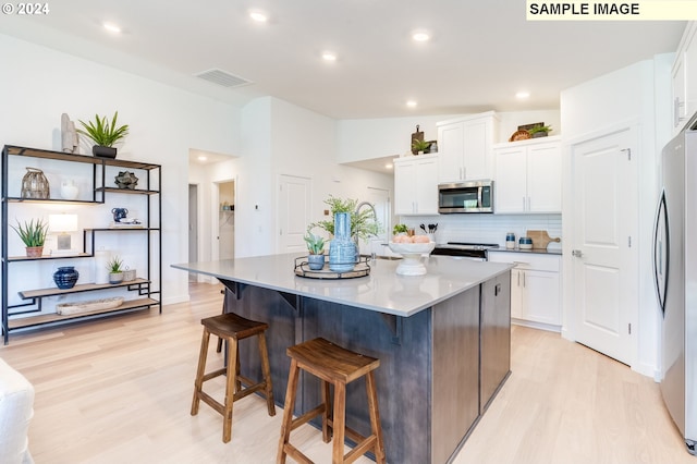 kitchen with light wood finished floors, visible vents, appliances with stainless steel finishes, white cabinets, and a kitchen bar