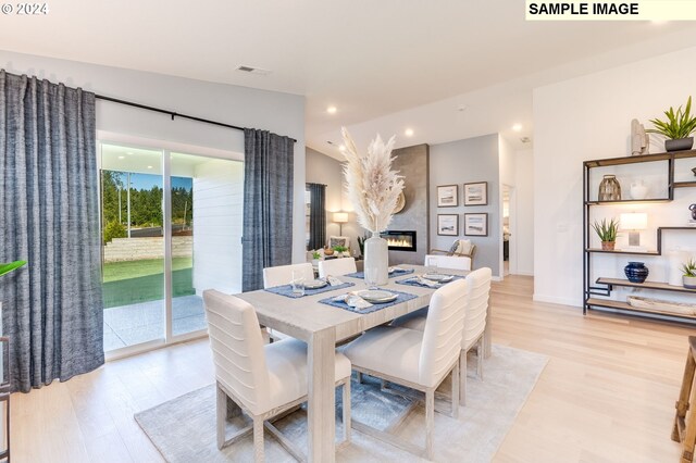 dining area with vaulted ceiling, light wood finished floors, a fireplace, and visible vents