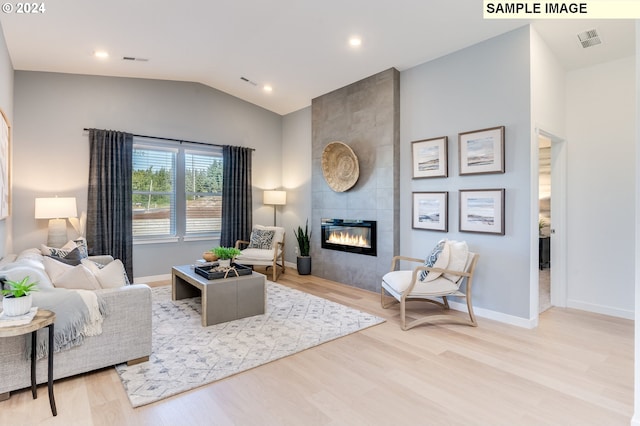 living room featuring a tiled fireplace, lofted ceiling, and light hardwood / wood-style flooring