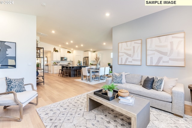 living area featuring baseboards, visible vents, lofted ceiling, light wood-style floors, and recessed lighting